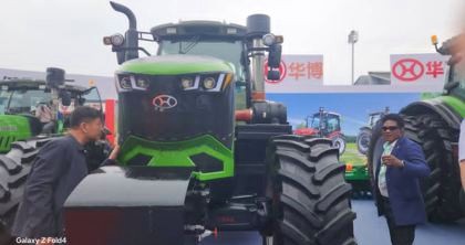 KCCIMA delegate beside a large green tractor at an outdoor agricultural machinery exhibition